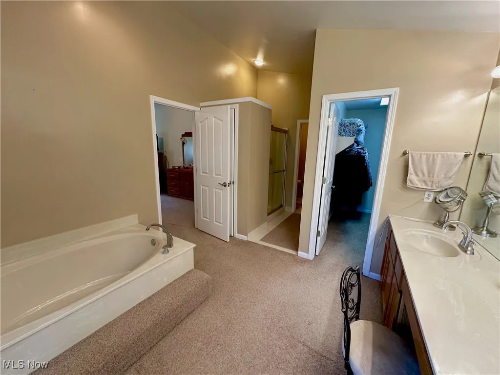 Ensuite bathroom with lofted ceiling, a bath, and large vanity