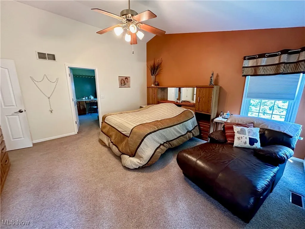 Primary Bedroom with carpet flooring, ensuite bath, ceiling fan, and high vaulted ceiling