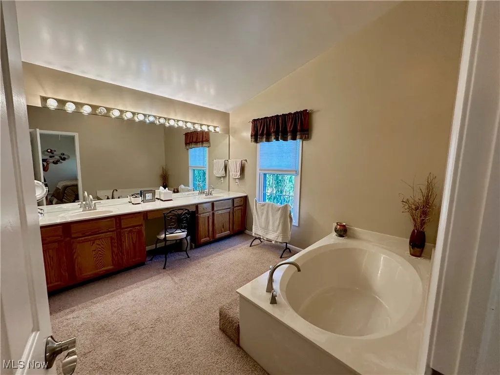 Ensuite bathroom with lofted ceiling, a bath, and large vanity