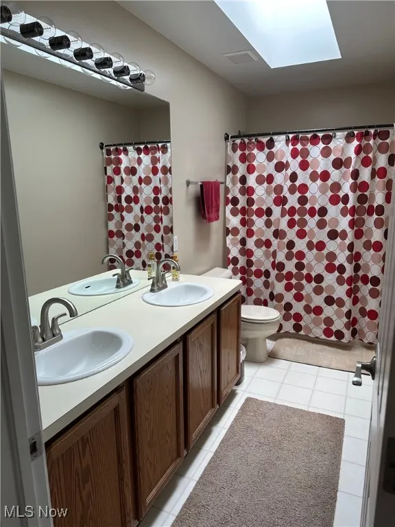 Full bathroom featuring double vanity, a skylight, light tile patterned flooring, and a shower with shower curtain