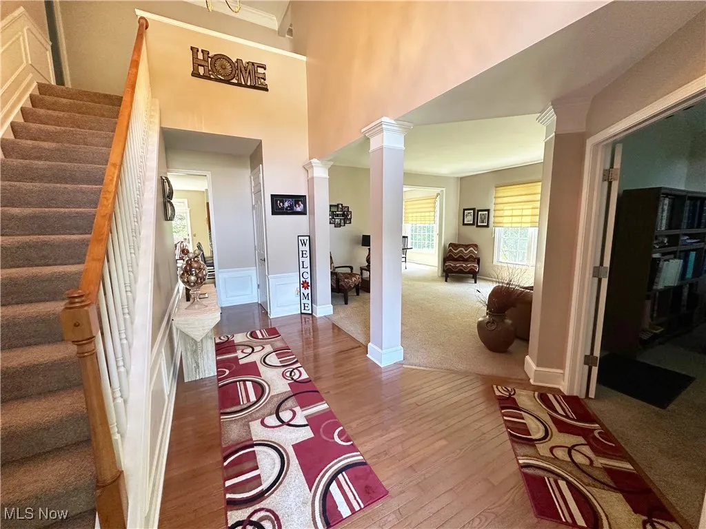 Entrance foyer with stairway, light wood-style flooring, a towering ceiling, decorative columns, and light colored carpet