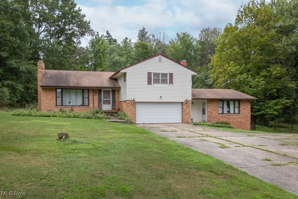 Split level home with a chimney, an attached garage, driveway, and brick siding