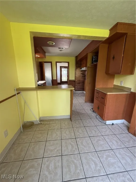 Kitchen with brown cabinetry, light tile patterned floors, and a peninsula