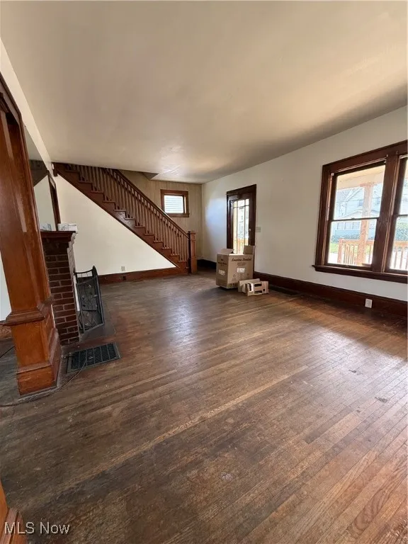 Unfurnished living room featuring dark wood-type flooring, plenty of natural light, and a fireplace