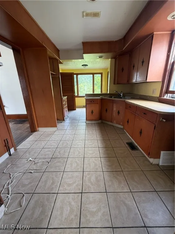 Kitchen featuring a peninsula, light tile patterned floors, open shelves, and brown cabinetry