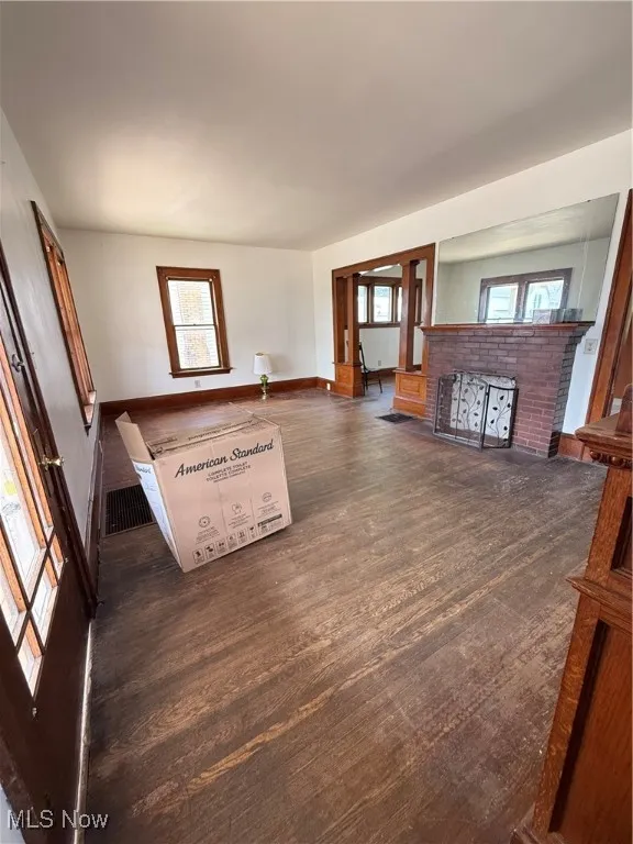 Unfurnished living room featuring dark wood-style flooring and baseboards