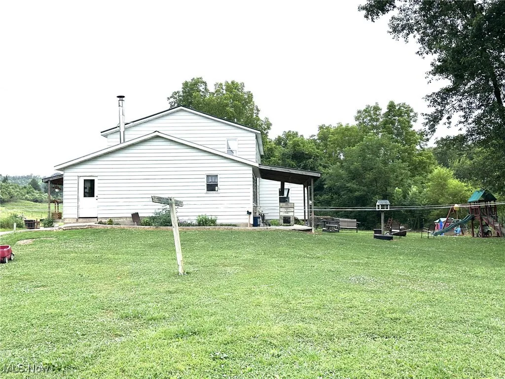 Rear view of house featuring a playground, a lawn, and view of wooded area