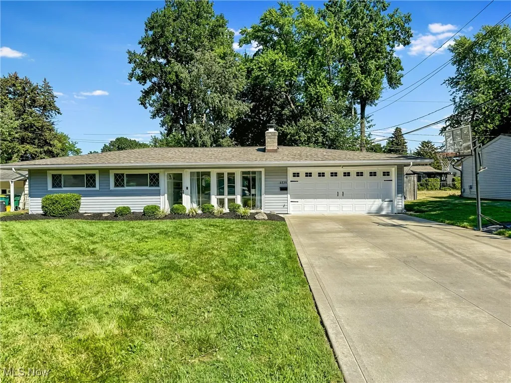 Ranch-style house featuring a garage, a front yard, a chimney, concrete driveway, and a shingled roof