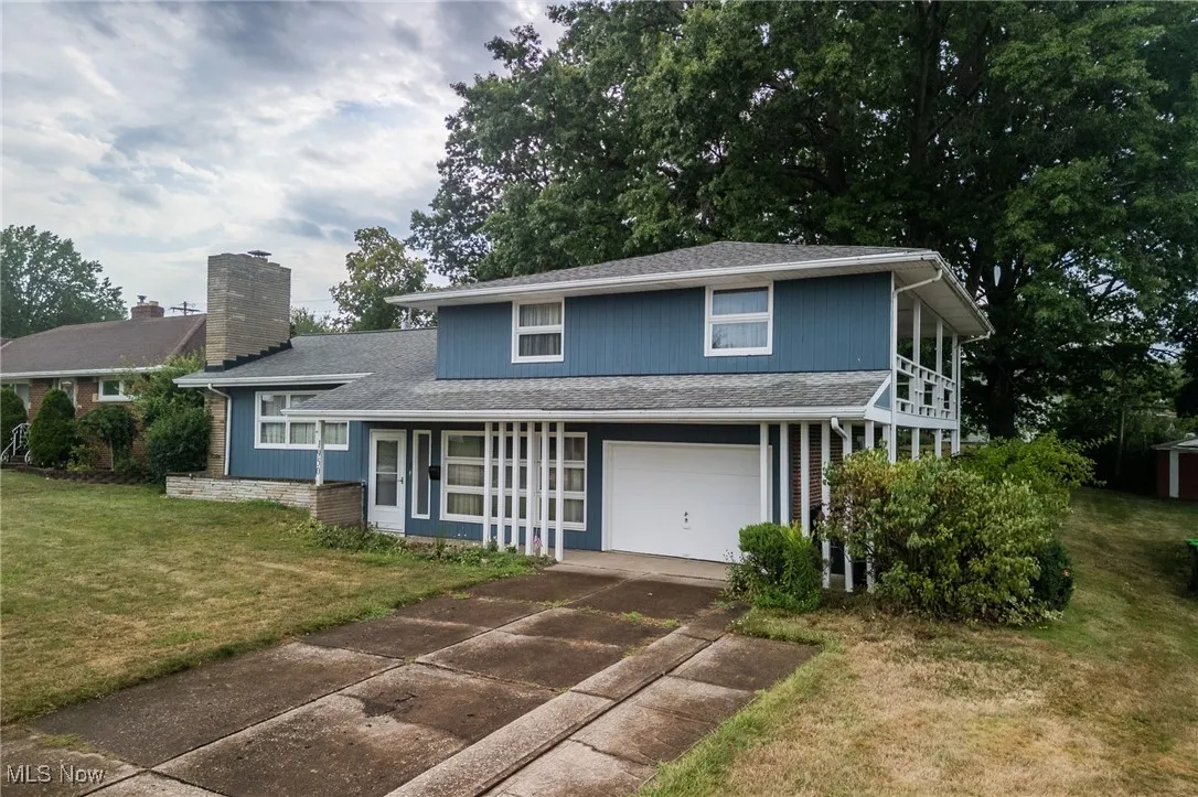 View of front of home with an attached garage, a front lawn, driveway, a chimney, and roof with shingles