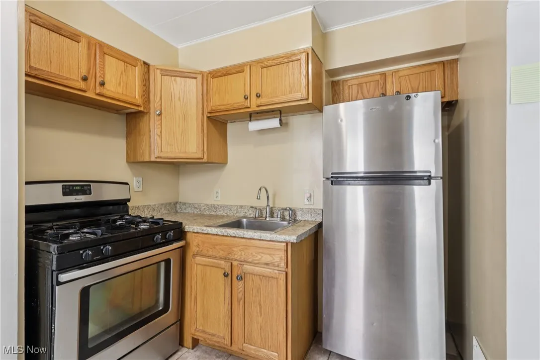 Kithcen with sink, stove, refrigerator and tile flooring.
