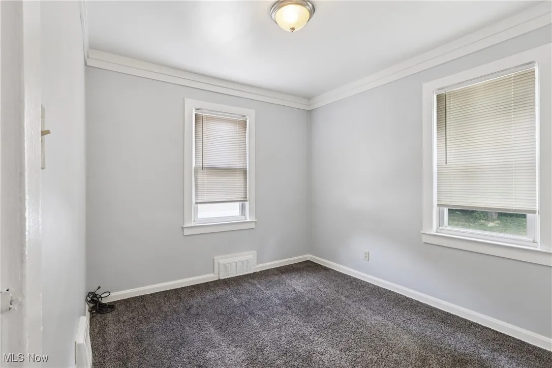 Spare room featuring dark colored carpet and crown molding