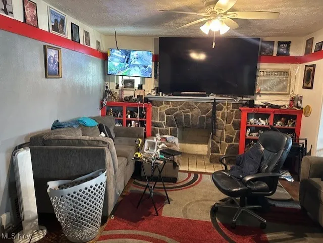 Living room with a textured ceiling, ceiling fan, and a stone fireplace