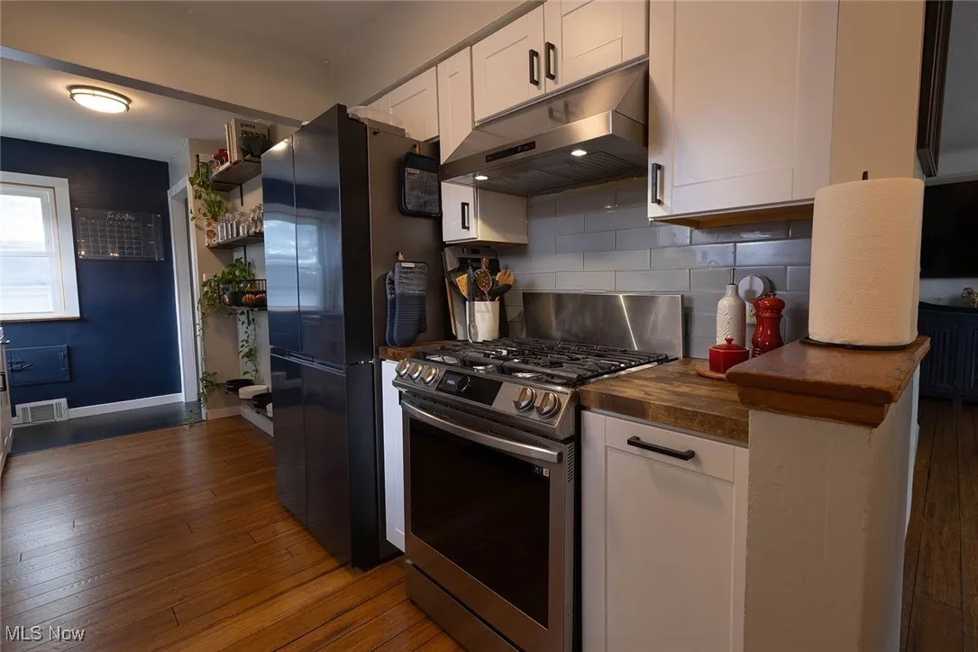 Kitchen featuring white cabinets, stainless steel appliances, under cabinet range hood, and tasteful backsplash