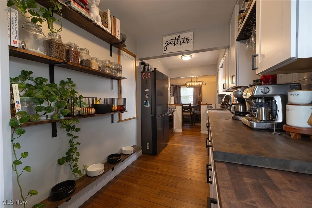 Kitchen featuring wooden counters, freestanding refrigerator, wood flooring, and white cabinets