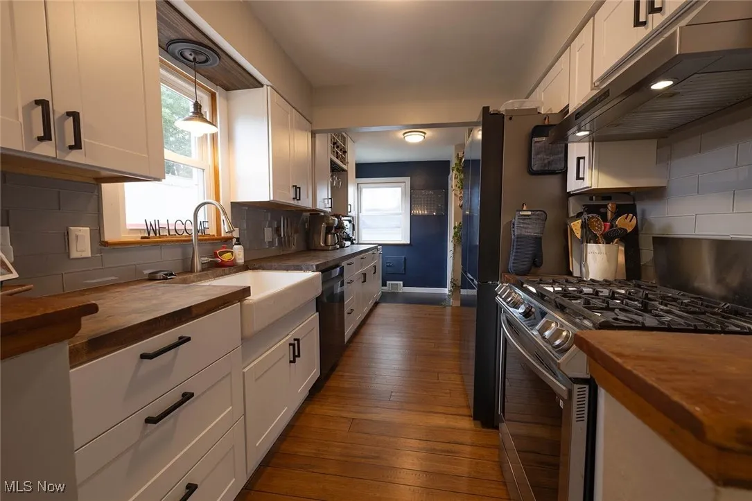 Kitchen with backsplash, butcher block countertops, white cabinets, and stainless steel appliances