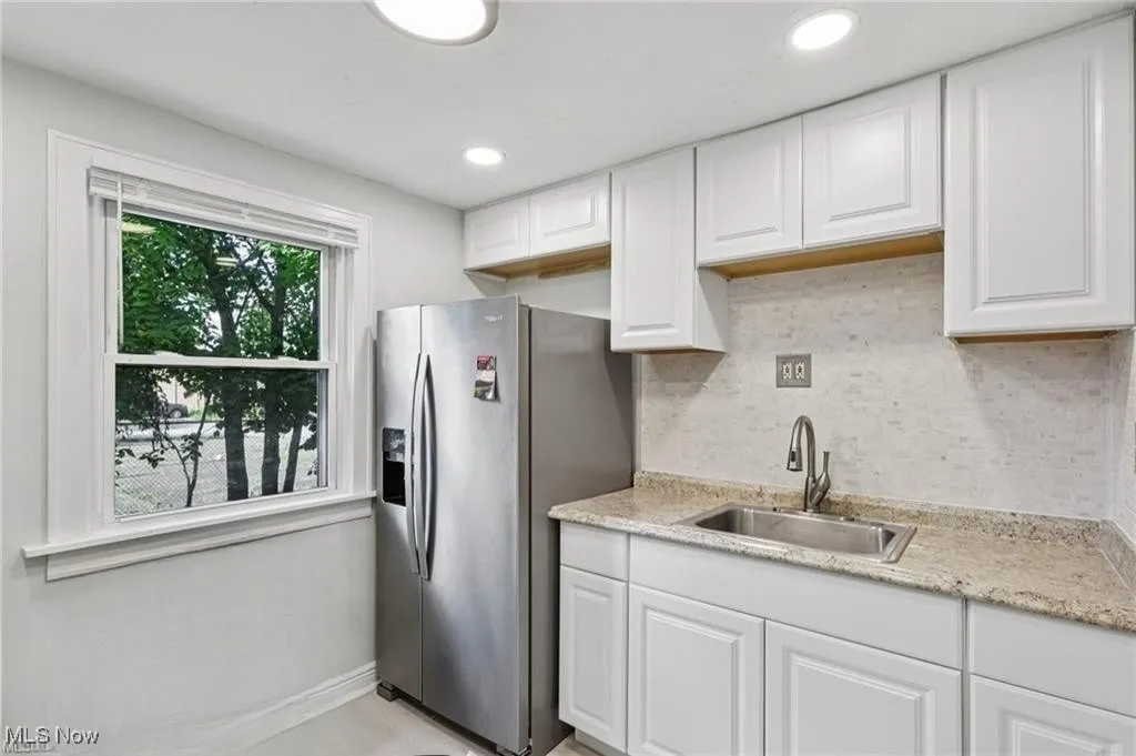 Kitchen with white cabinetry, stainless steel fridge with ice dispenser, backsplash, light stone counters, and recessed lighting