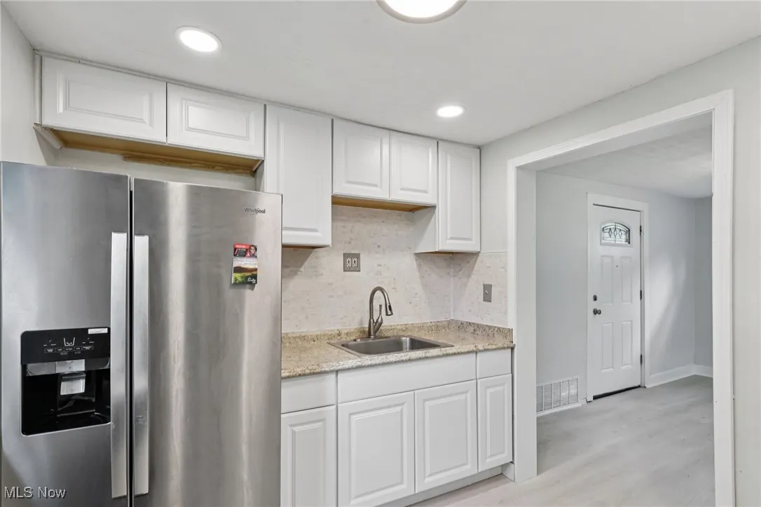 Kitchen featuring stainless steel fridge, white cabinets, tasteful backsplash, recessed lighting, and light stone counters