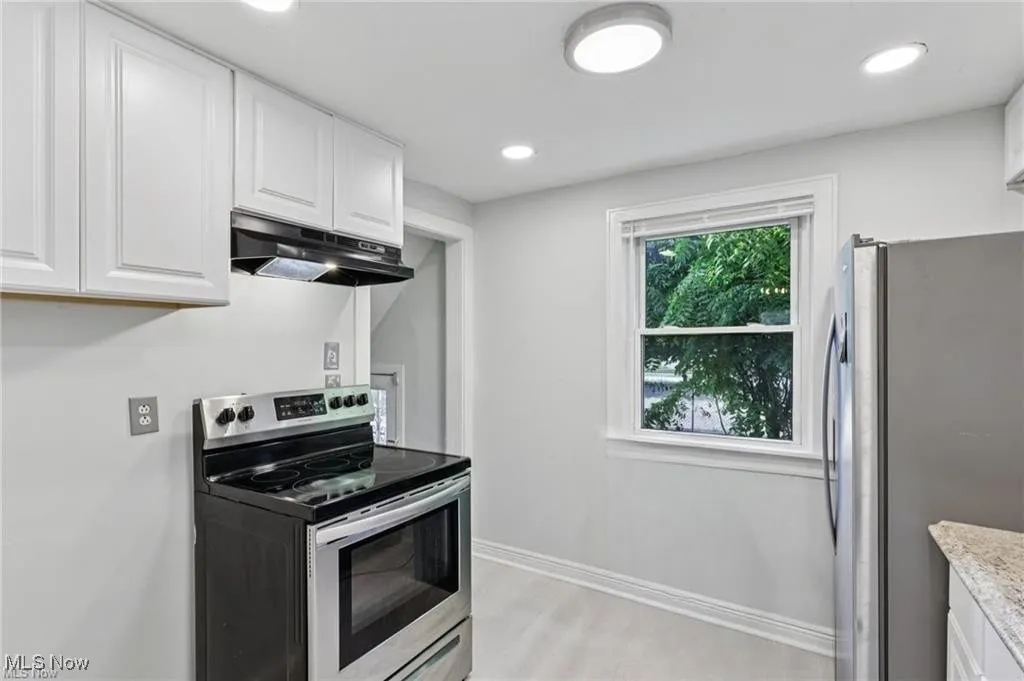 Kitchen featuring stainless steel appliances, white cabinets, under cabinet range hood, recessed lighting, and light stone counters