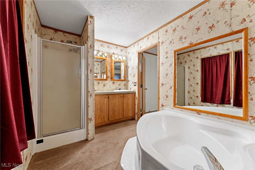 Full bath with wallpapered walls, a shower stall, a garden tub, vanity, and a textured ceiling