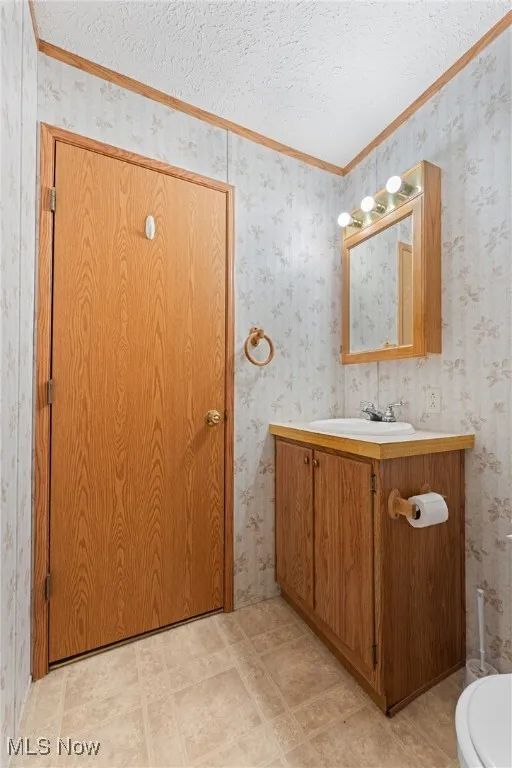Half bathroom featuring wallpapered walls, vanity, a textured ceiling, and crown molding