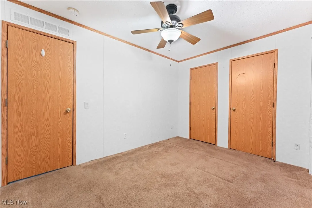 Unfurnished bedroom featuring ornamental molding, multiple closets, carpet, and ceiling fan