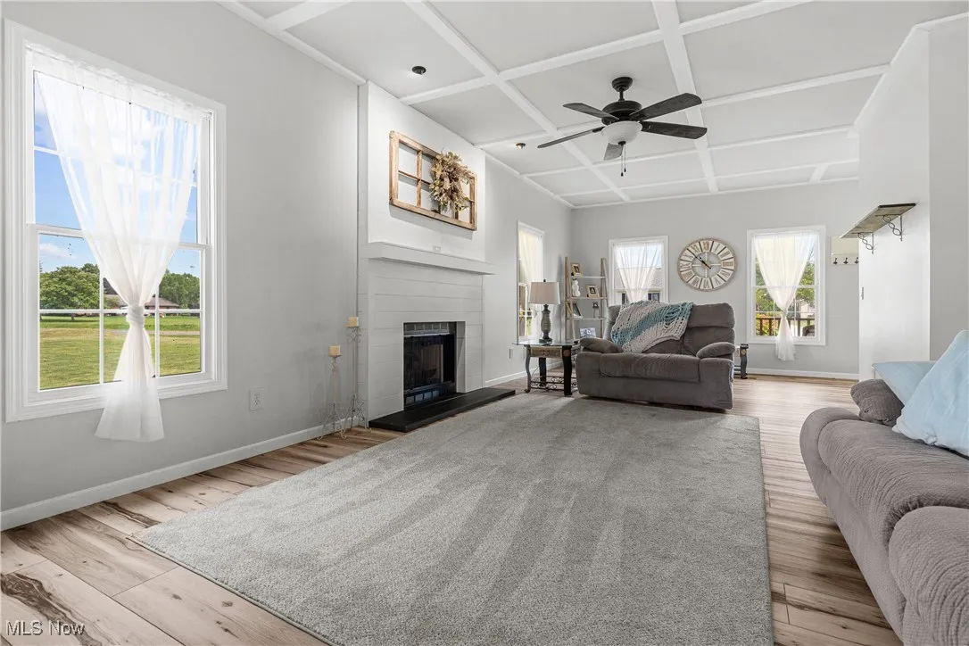 Living area featuring coffered ceiling, wood finished floors, a fireplace, ceiling fan, and beamed ceiling