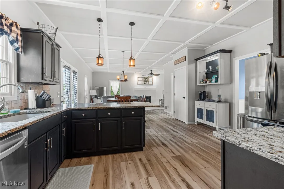 Kitchen with stainless steel appliances, a ceiling fan, light wood-style floors, tasteful backsplash, and coffered ceiling
