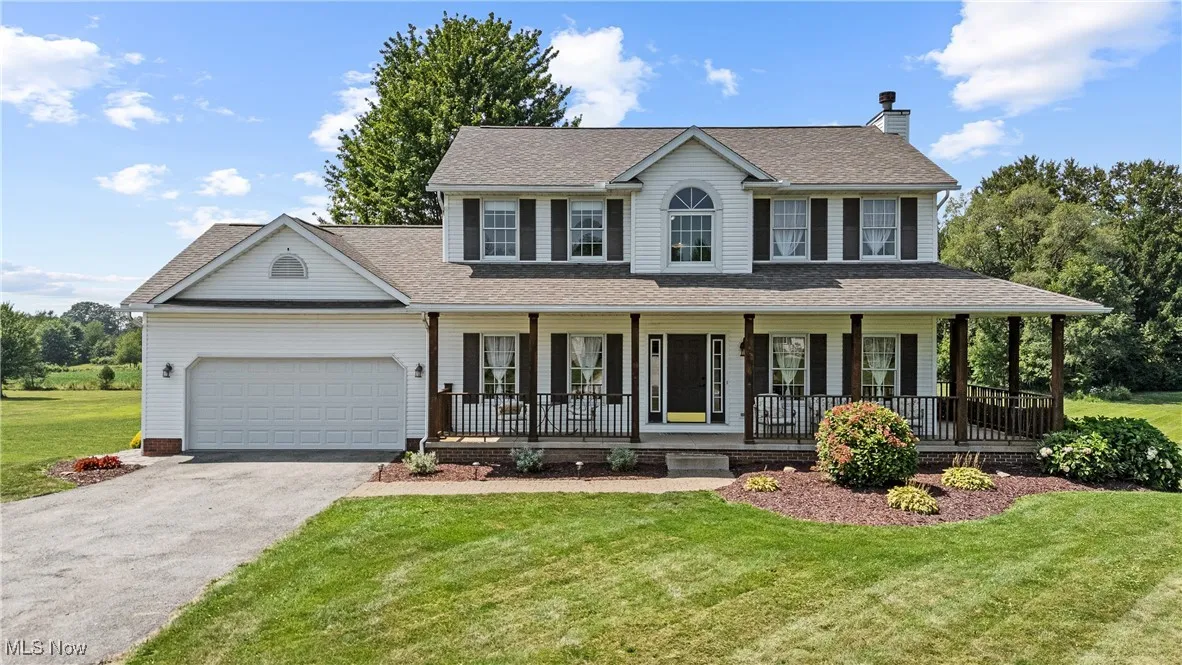Colonial-style house with a front yard, a chimney, asphalt driveway, a shingled roof, and an attached garage