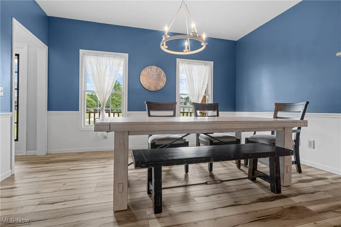 Dining room featuring a chandelier, plenty of natural light, light wood-type flooring, and a wainscoted wall