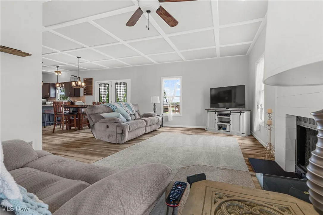 Living area with a ceiling fan, coffered ceiling, wood finished floors, and a tile fireplace