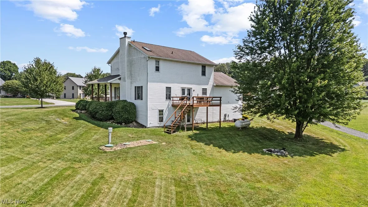 Rear view of house featuring a wooden deck, a yard, stairs, and a chimney