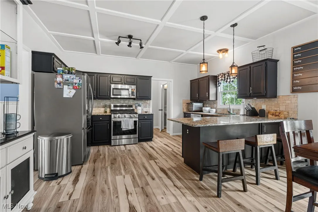 Kitchen with a peninsula, stainless steel appliances, decorative backsplash, light wood-style flooring, and light stone countertops