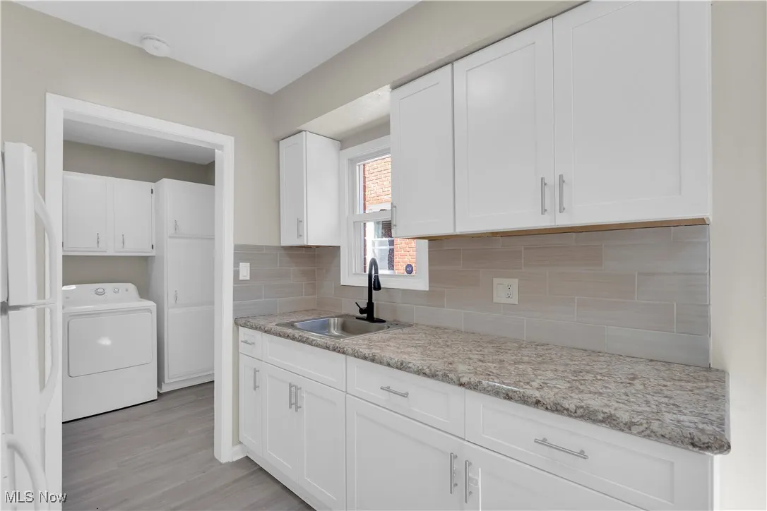 Kitchen featuring washer / dryer, freestanding refrigerator, white cabinetry, backsplash, and light wood-type flooring