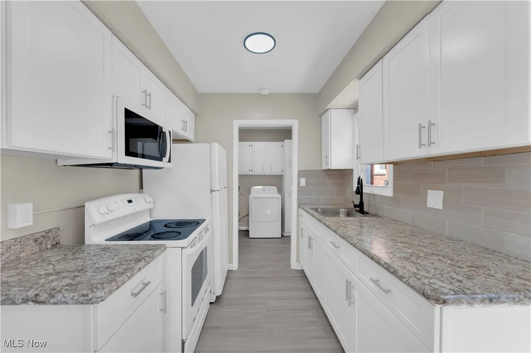Kitchen featuring white appliances, white cabinetry, washer / dryer, and light countertops