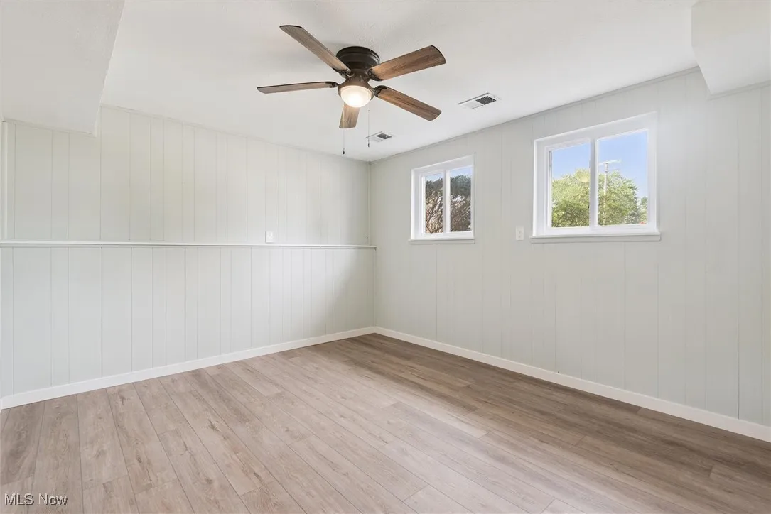 Empty room featuring a ceiling fan, light wood finished floors, and wooden walls