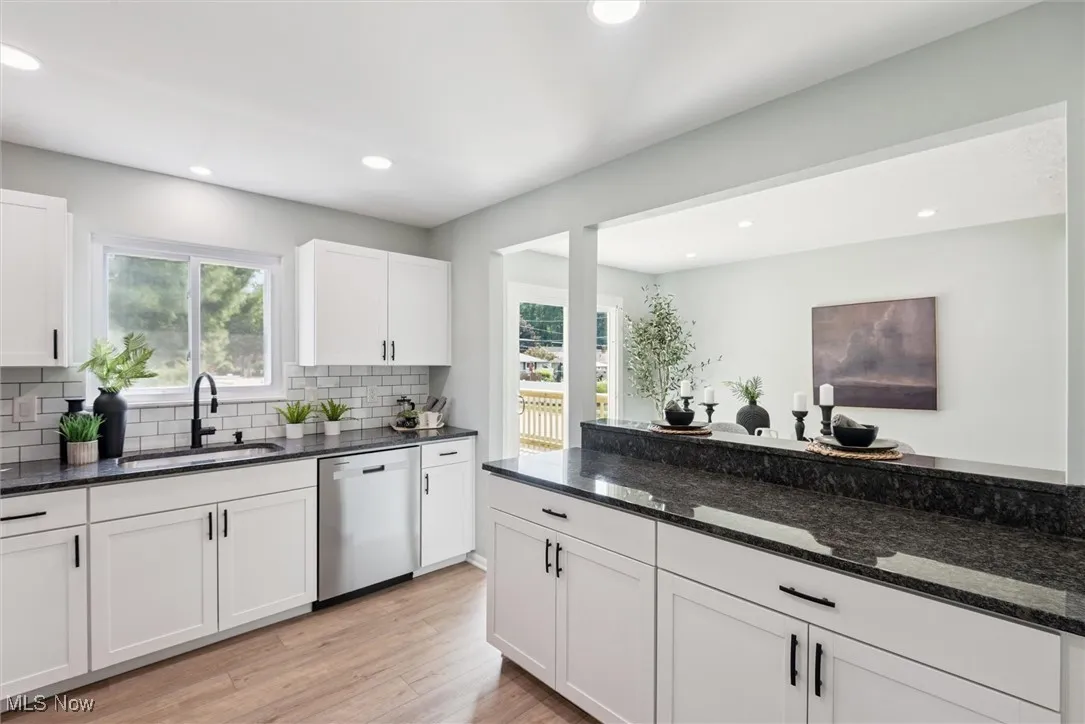 Kitchen with dark stone countertops, white cabinets, dishwasher, light wood-style floors, and backsplash