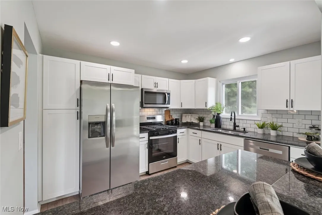 Kitchen featuring appliances with stainless steel finishes, white cabinets, dark stone counters, backsplash, and recessed lighting