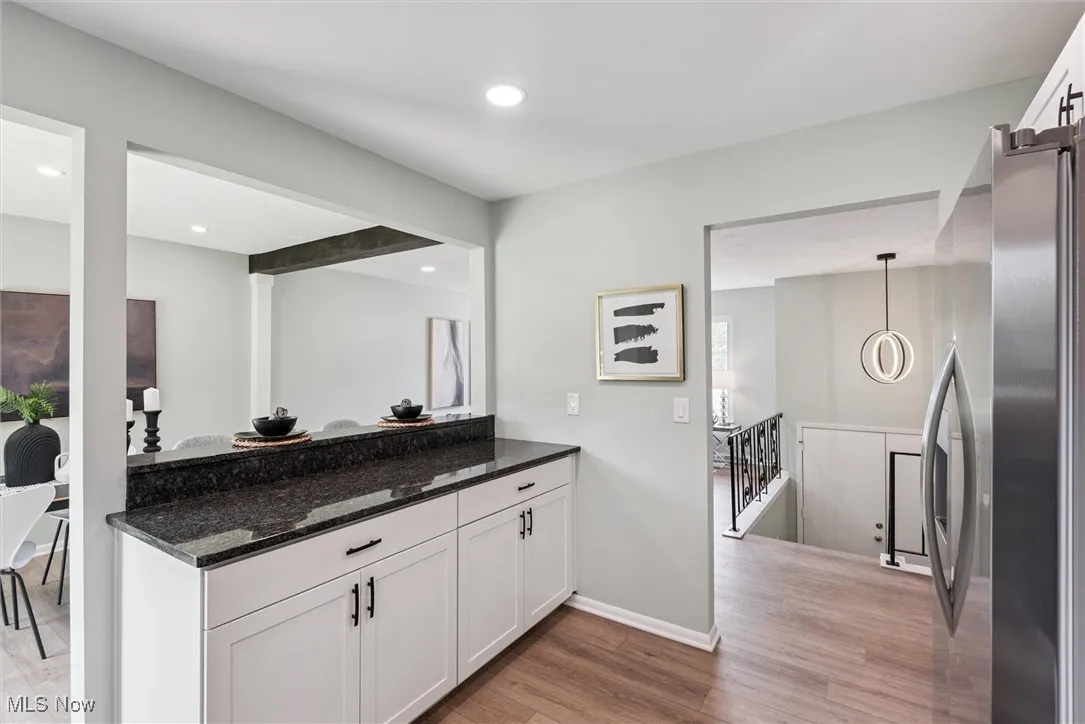 Kitchen featuring dark stone counters, white cabinets, stainless steel fridge with ice dispenser, light wood-type flooring, and recessed lighting