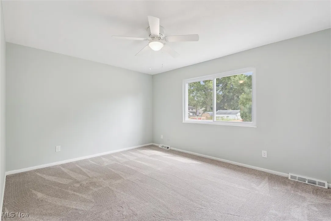 Empty room with light carpet and a ceiling fan