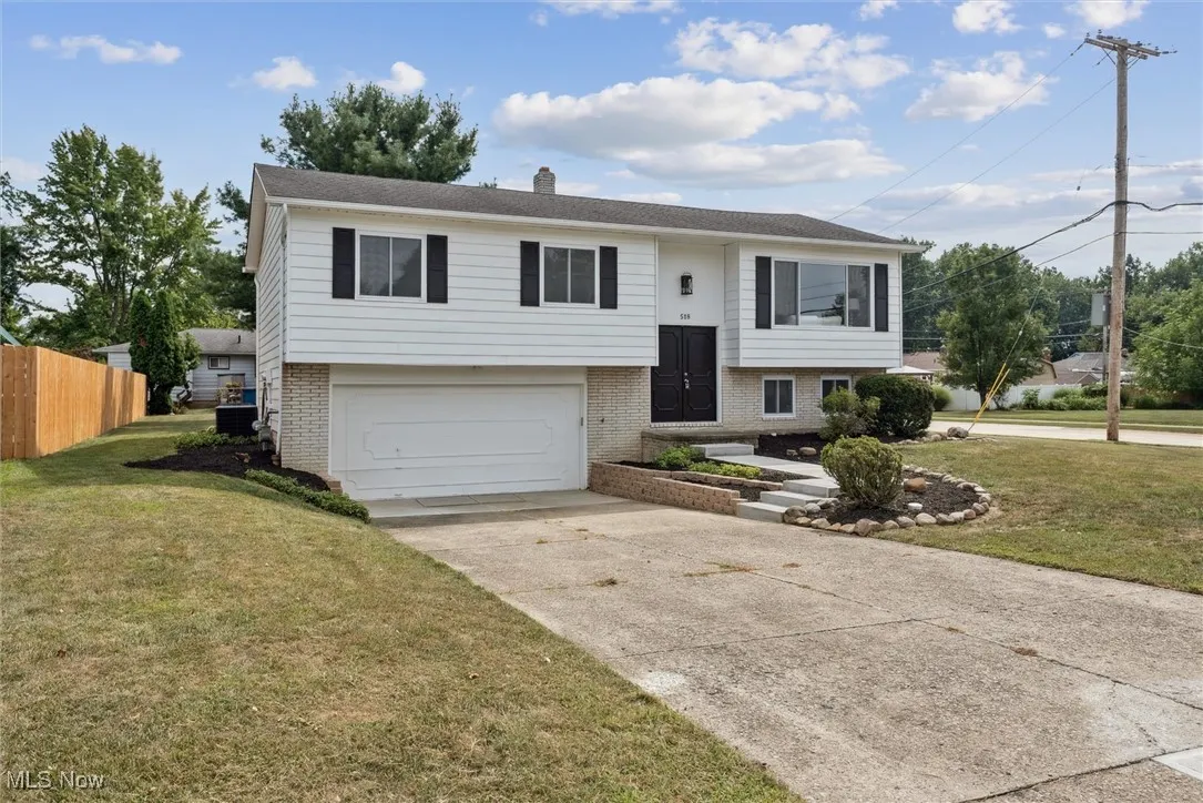 Split foyer home with brick siding, an attached garage, driveway, and a chimney