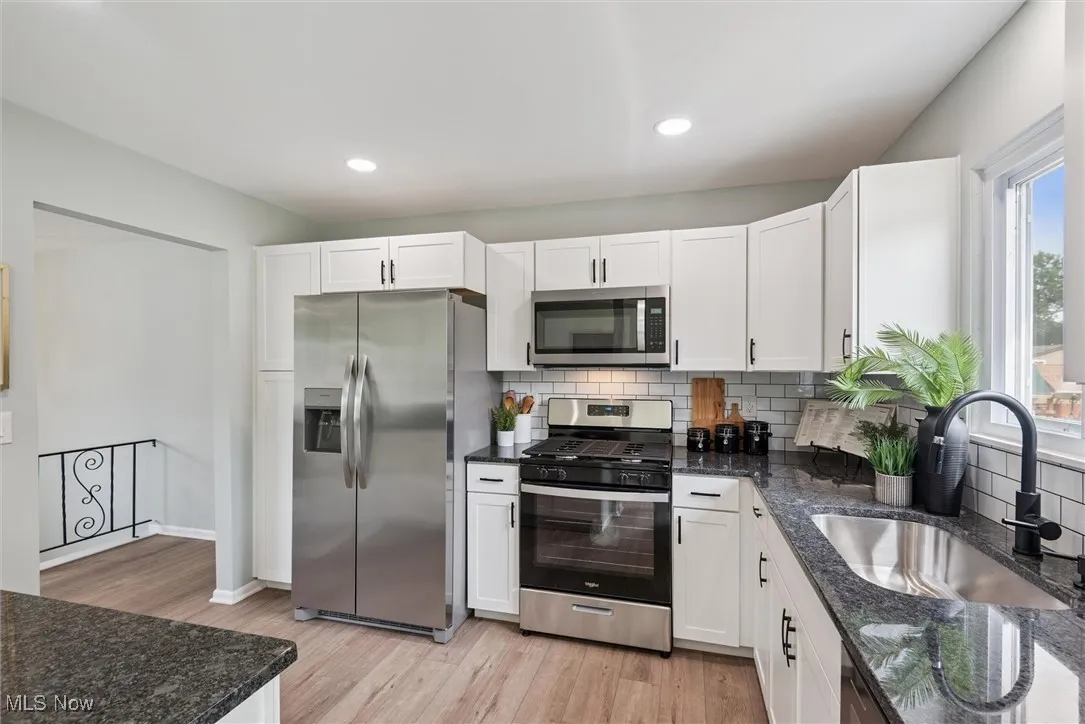 Kitchen with dark stone countertops, decorative backsplash, stainless steel appliances, white cabinets, and recessed lighting