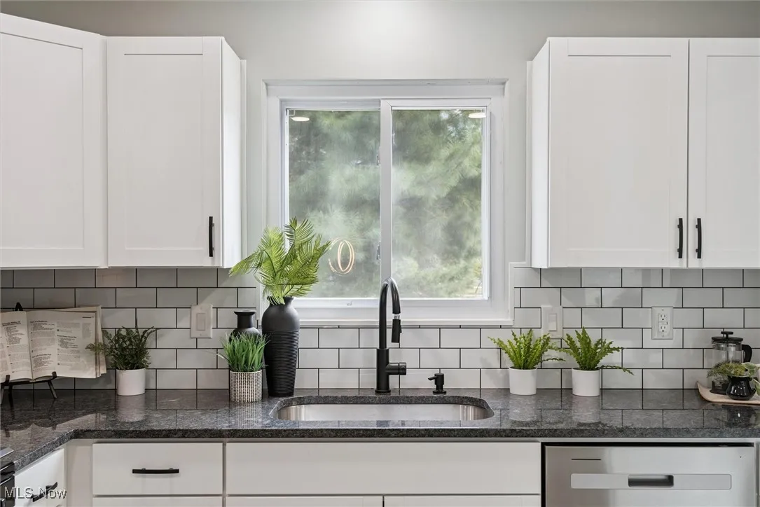 Kitchen featuring white cabinets, dark stone counters, and backsplash
