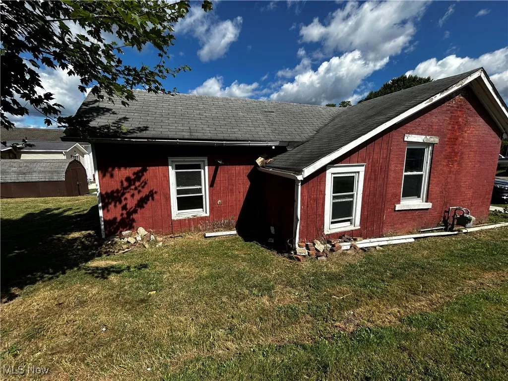 Rear view of house featuring a shingled roof and a lawn