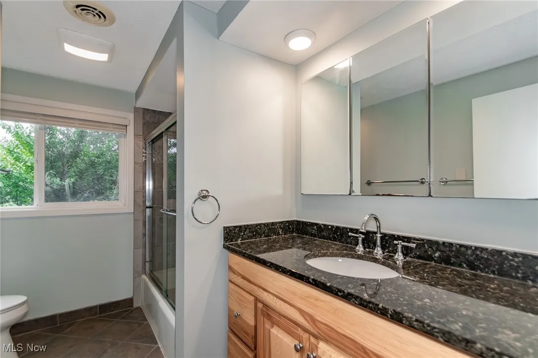 Bathroom with vanity, shower / bath combination with glass door, and dark tile patterned flooring