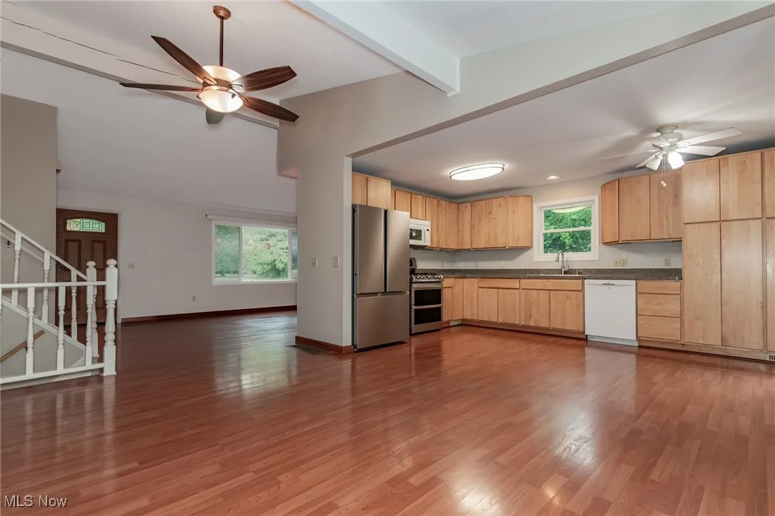 Kitchen with ceiling fan, light brown cabinetry, beam ceiling, dark countertops, and appliances with stainless steel finishes