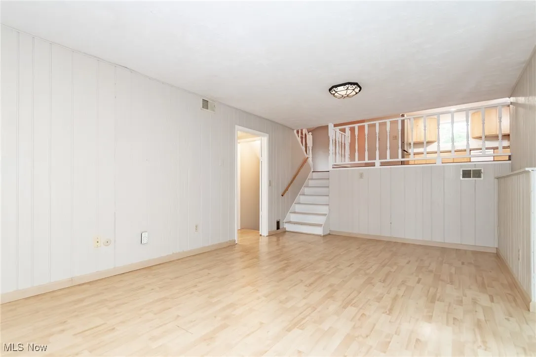 Unfurnished living room featuring light wood-style floors, stairs, and wood walls