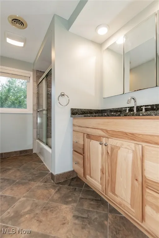 Bathroom with vanity, combined bath / shower with glass door, and dark stone finish flooring