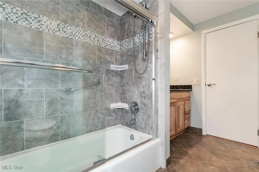 Bathroom with bath / shower combo with glass door and vanity