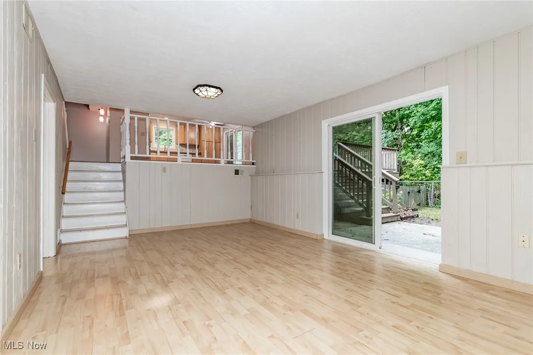 Unfurnished living room featuring stairs, light wood-style floors, and wooden walls