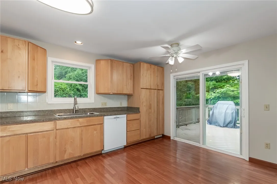 Kitchen with light brown cabinetry, light wood-style flooring, dark countertops, dishwasher, and recessed lighting